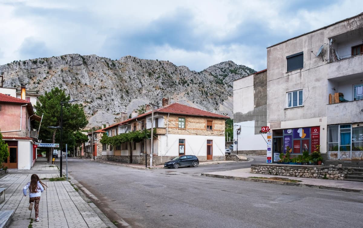Picturesque village street in Albania with classic architecture framed by rugged mountains.