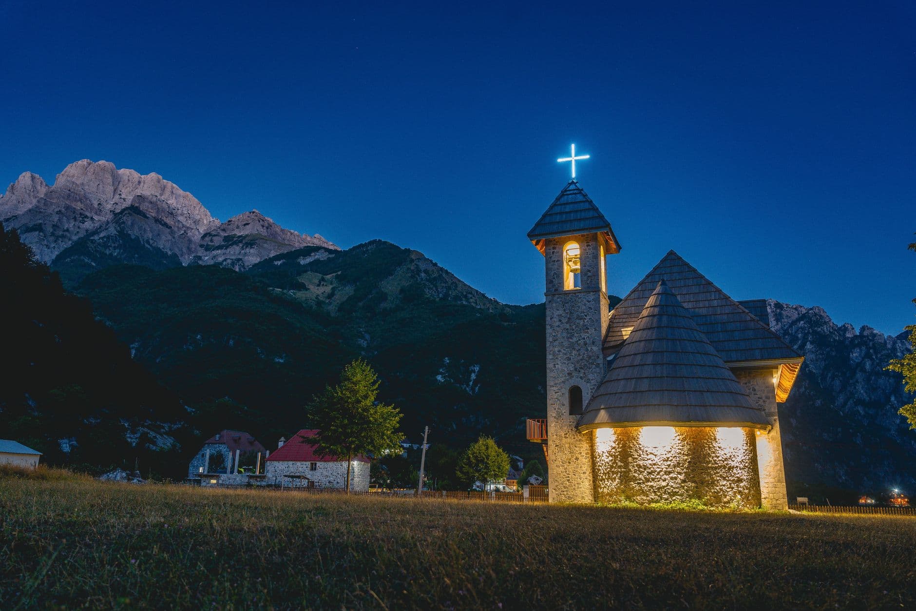 La petite église blanche de Theth dans sa prairie, cernée par les parois calcaires des Alpes albanaises